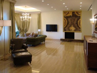 SALONE. Pavimento realizzato in marmo. Camino con pannello decorativo in onice. Divani e poltrone rivestiti in camoscio (BAXTER). Lampadario, applique e lampada da terra con finitura oro (DE MAJO). 