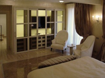 CAMERA PADRONALE. Arredamento personalizzato con zona TV ed illuminazione integrata con sensore a movimento (BEZUS - LPL). Poltrone rivestite in velluto (MINOTTI COLLEZIONI). Tavolino in marmo con base in ottone satinato (MINOTTI COLLEZIONI).