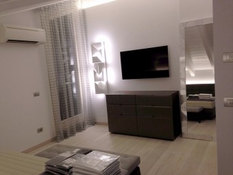 CAMERA PADRONALE. Soffitto con travi a vista. Pavimento in parquet Spazzolato Rovere Argento. Comò tailor made (BEZUS - LPL). Specchio personalizzato con finitura argento (BEZUS - LPL). Lampada a parete Wall Shadows Long (NEMO).